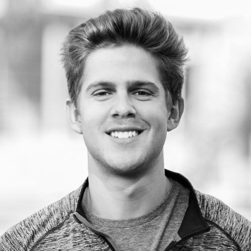 Portrait of a man with brown hair and glasses on a flat gray background.